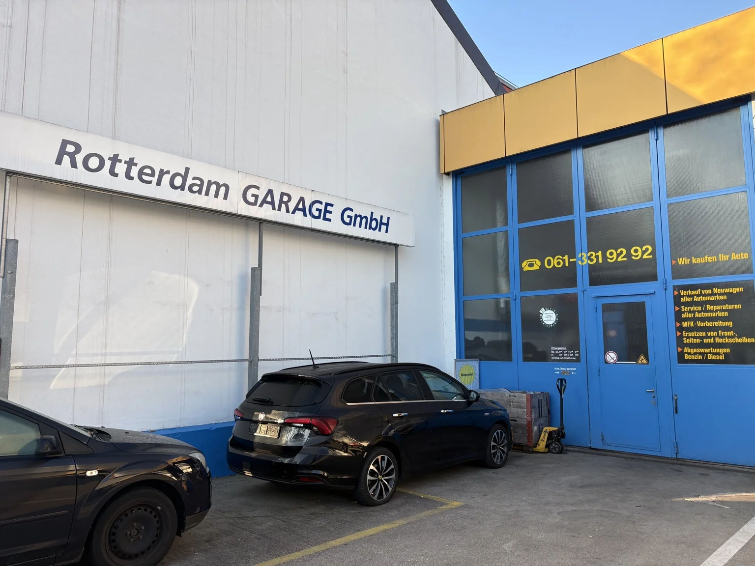 Haupteingang der Rotterdam Garage GmbH mit blauem Tor, Firmenschriftzug und Fahrzeugen davor